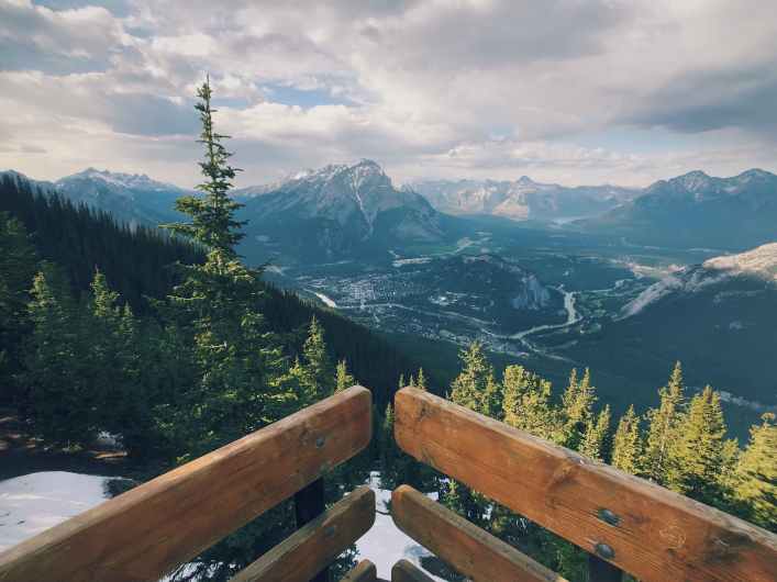 Scenic mountain view of Banff town and Bow Valley from a wooden lookout deck surrounded by pines
