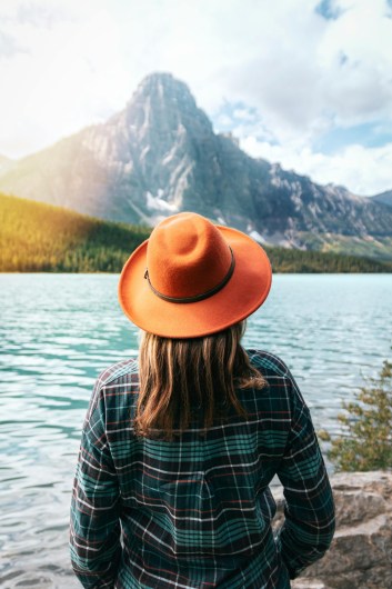 Traveler in an orange hat admires the turquoise lake and mountain views in Banff National Park.