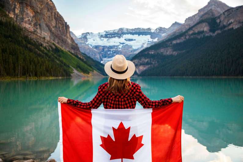 Woman holding Canadian flag overlooking turquoise Lake Louise and mountains in Banff National Park