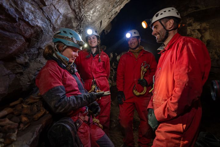 Adventurers explore a Banff cave in red suits, sharing smiles under the glow of helmet lights.