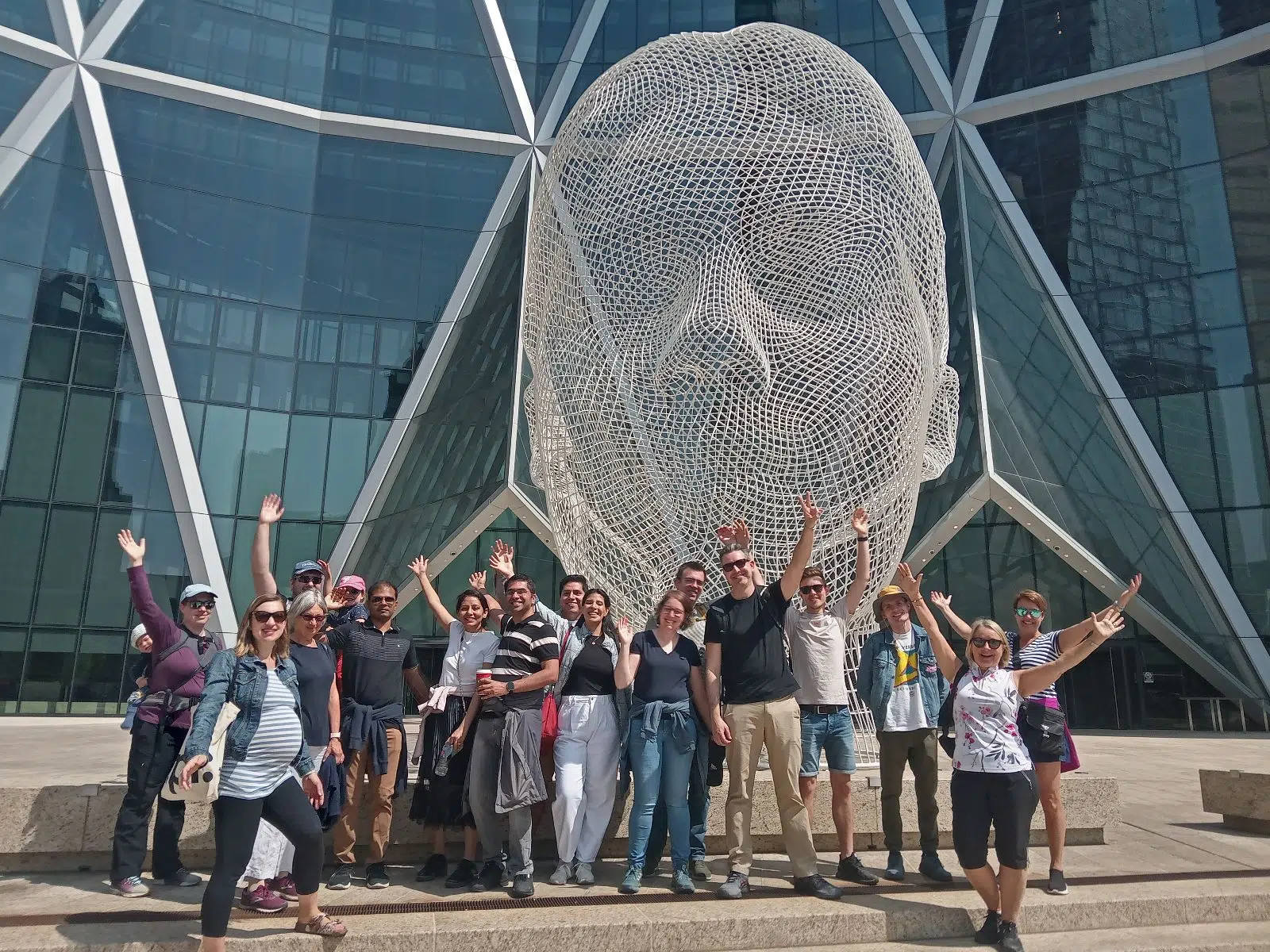Tour group posing and waving in front of Wonderland Wire Head sculpture during Calgary walking tour