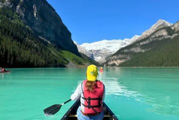 Woman paddling canoe on turquoise Lake Louise surrounded by mountains in Banff National Park