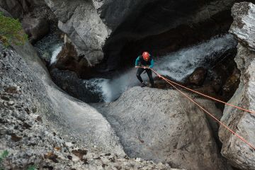 Person rappelling down rocky canyon beside waterfall during Heart Creek Canyon adventure in Banff